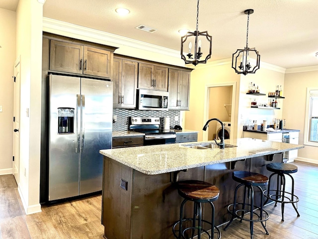 kitchen featuring light stone countertops, dark brown cabinets, stainless steel appliances, a kitchen island with sink, and sink