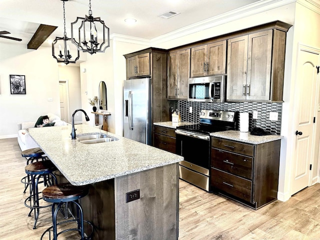 kitchen featuring light stone countertops, stainless steel appliances, beam ceiling, a breakfast bar area, and an island with sink