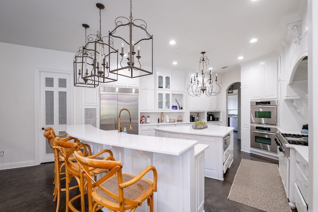 kitchen with pendant lighting, a breakfast bar, a center island with sink, white cabinets, and built in appliances