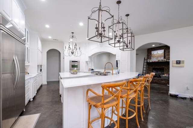 kitchen featuring pendant lighting, an island with sink, stainless steel appliances, and a brick fireplace