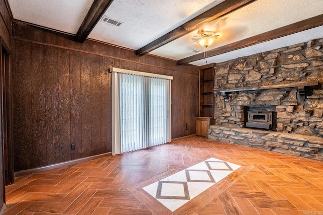 unfurnished living room with parquet floors, a wood stove, wooden walls, a textured ceiling, and beamed ceiling