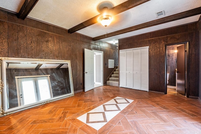 unfurnished bedroom featuring wooden walls, beamed ceiling, parquet floors, and ceiling fan