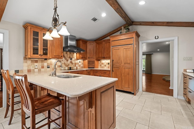 kitchen featuring kitchen peninsula, a kitchen breakfast bar, wall chimney range hood, pendant lighting, and vaulted ceiling with beams