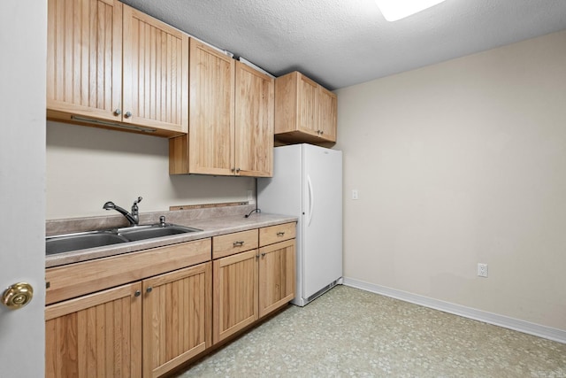 kitchen with light brown cabinetry, sink, white fridge, and a textured ceiling