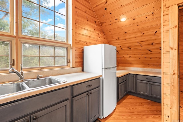 kitchen with sink, wooden walls, white fridge, light hardwood / wood-style floors, and wood ceiling