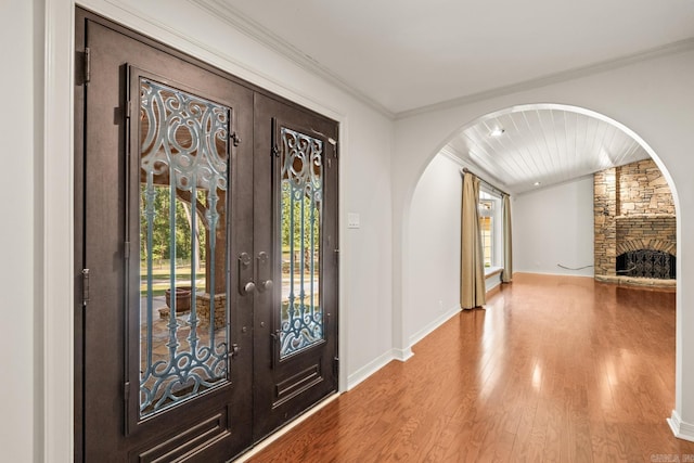 entryway featuring a stone fireplace, crown molding, french doors, and hardwood / wood-style floors