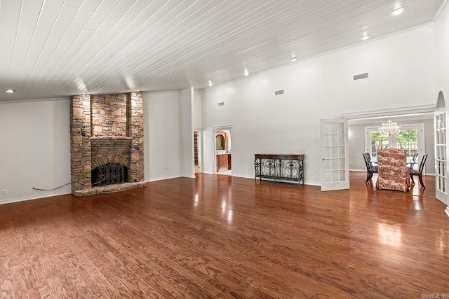 unfurnished living room featuring french doors, a stone fireplace, a chandelier, hardwood / wood-style flooring, and ornamental molding