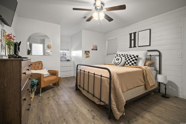 bedroom featuring ceiling fan, visible vents, wooden walls, and wood finished floors