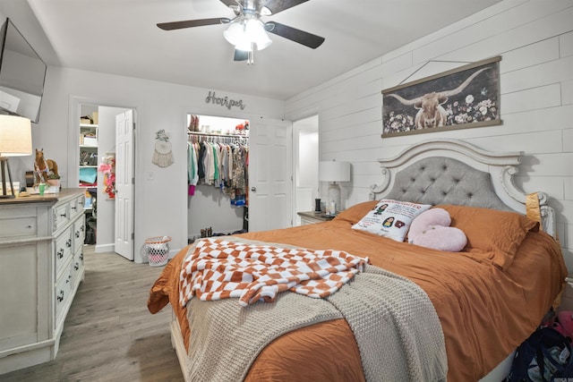 bedroom with wood walls, a walk in closet, dark hardwood / wood-style floors, ceiling fan, and a closet