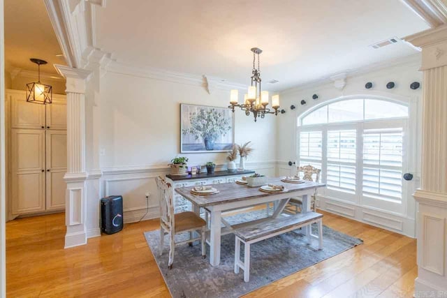 dining space featuring ornate columns, light wood-type flooring, a notable chandelier, and ornamental molding