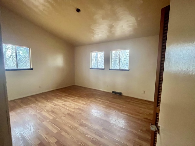 spare room with hardwood / wood-style floors and vaulted ceiling