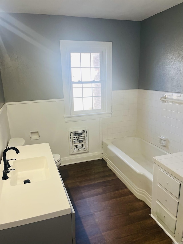 bathroom featuring a tub to relax in, vanity, heating unit, hardwood / wood-style floors, and toilet