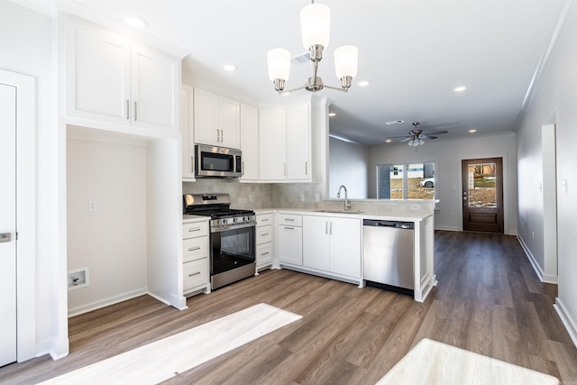 kitchen with ceiling fan with notable chandelier, stainless steel appliances, sink, pendant lighting, and white cabinetry