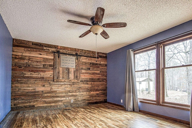 empty room featuring ceiling fan, wooden walls, hardwood / wood-style floors, and a textured ceiling