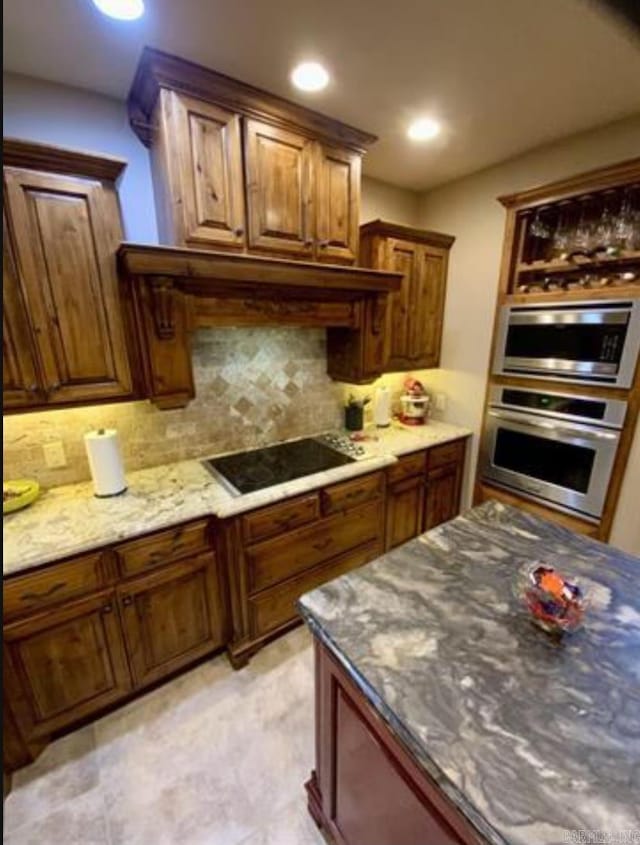 kitchen with decorative backsplash, black electric cooktop, stainless steel microwave, and dark stone counters