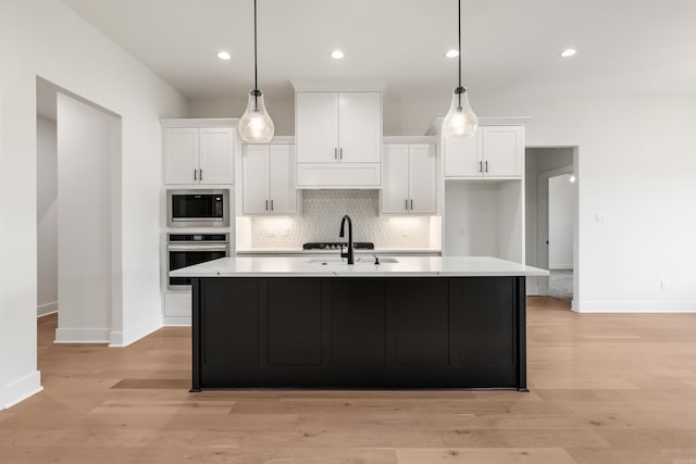 kitchen with an island with sink, white cabinetry, built in microwave, and stainless steel oven