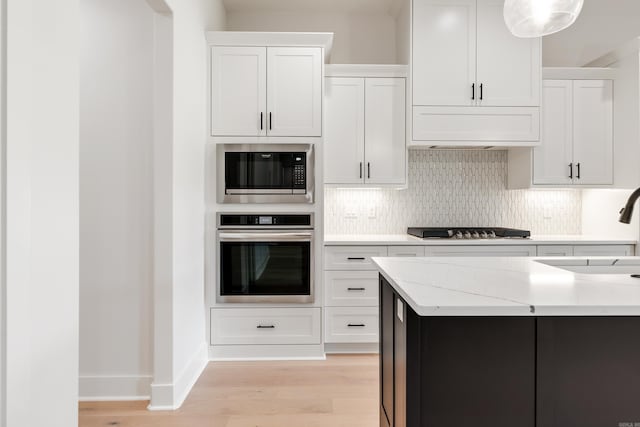 kitchen featuring light stone countertops, light wood-type flooring, tasteful backsplash, white cabinetry, and stainless steel appliances