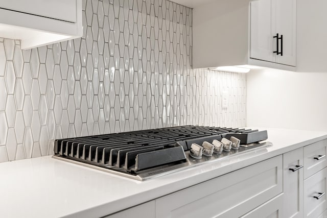 details featuring stainless steel gas stovetop, white cabinetry, and backsplash