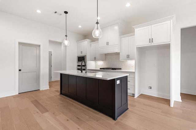 kitchen featuring built in microwave, sink, pendant lighting, a center island with sink, and white cabinets