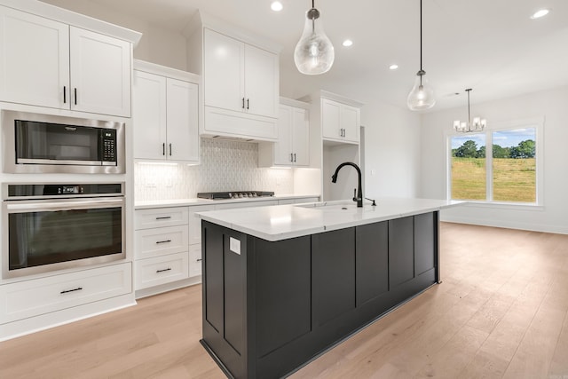 kitchen with stainless steel appliances, sink, pendant lighting, white cabinets, and an island with sink