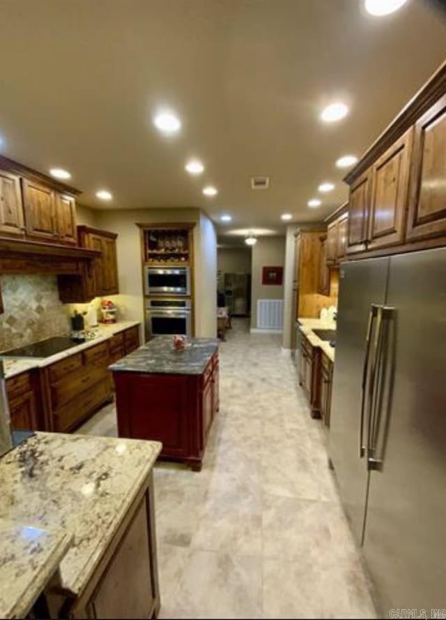 kitchen featuring light stone countertops, a center island, stainless steel appliances, and backsplash