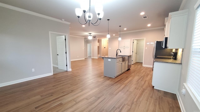 kitchen with white cabinets, ceiling fan with notable chandelier, an island with sink, and hanging light fixtures