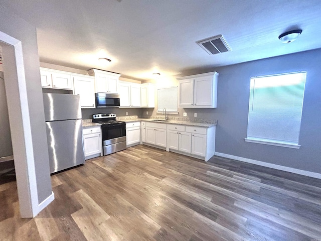 kitchen with light stone countertops, stainless steel appliances, sink, white cabinets, and dark hardwood / wood-style floors