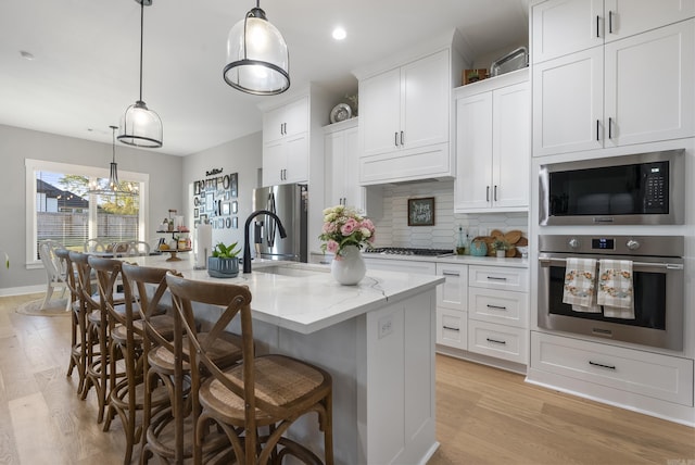 kitchen featuring appliances with stainless steel finishes, tasteful backsplash, hanging light fixtures, and an island with sink