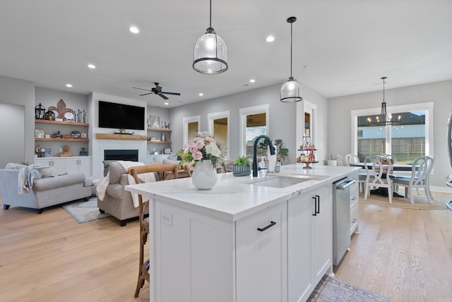 kitchen with white cabinets, decorative light fixtures, a center island with sink, and sink