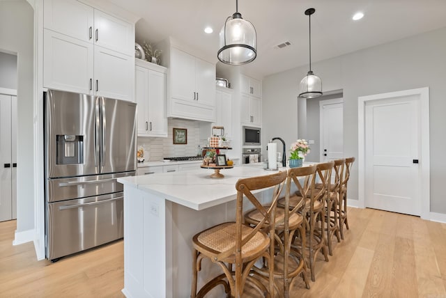 kitchen with white cabinetry, a center island with sink, pendant lighting, and appliances with stainless steel finishes