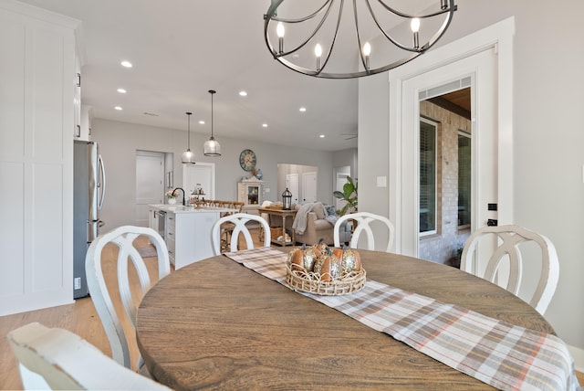 dining space featuring ceiling fan with notable chandelier, sink, and light hardwood / wood-style flooring