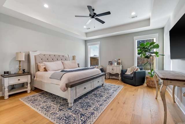 bedroom with ceiling fan, a raised ceiling, and light wood-type flooring