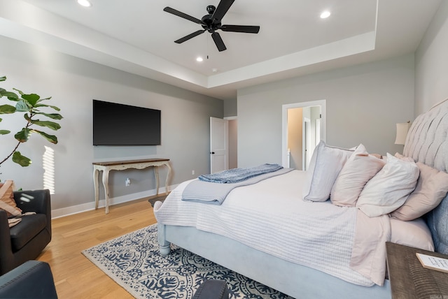 bedroom with ceiling fan, a tray ceiling, and light hardwood / wood-style flooring