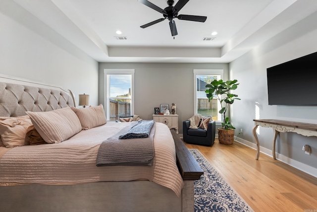 bedroom with ceiling fan, a raised ceiling, and light wood-type flooring