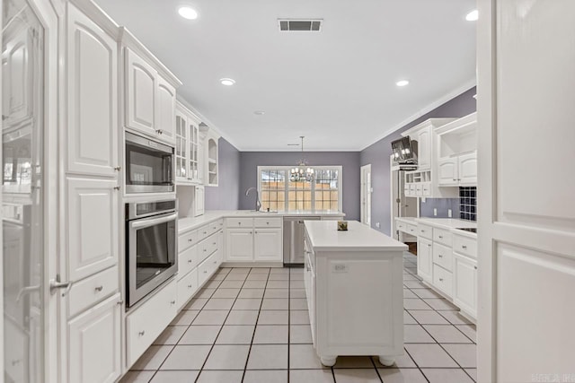 kitchen with appliances with stainless steel finishes, ornamental molding, a kitchen island, decorative light fixtures, and white cabinetry