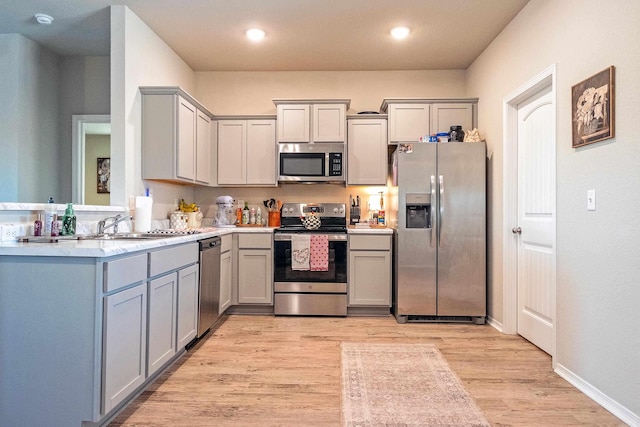 kitchen featuring kitchen peninsula, stainless steel appliances, sink, light hardwood / wood-style flooring, and gray cabinets