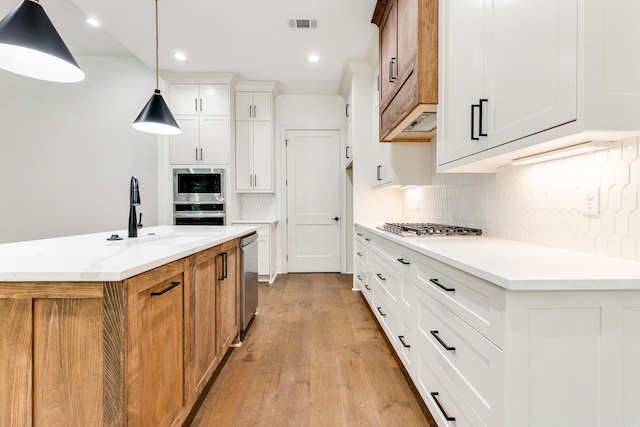 kitchen with sink, stainless steel appliances, an island with sink, pendant lighting, and white cabinets