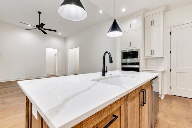 kitchen featuring decorative backsplash, light stone counters, a kitchen island with sink, sink, and white cabinets