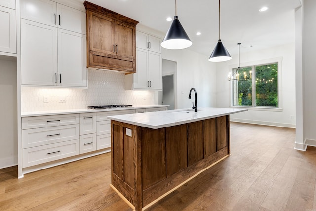 kitchen with a kitchen island with sink, sink, a notable chandelier, white cabinetry, and hanging light fixtures