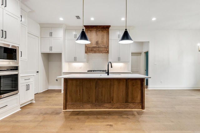 kitchen featuring pendant lighting, white cabinetry, an island with sink, and stainless steel appliances