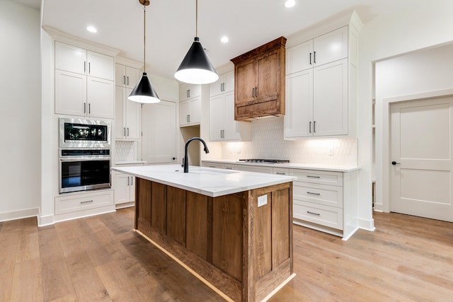 kitchen featuring white cabinets, sink, hanging light fixtures, an island with sink, and stainless steel appliances