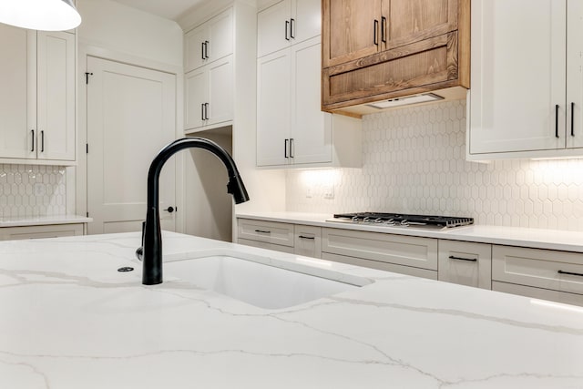 kitchen with stainless steel gas stovetop, light stone counters, white cabinetry, and sink