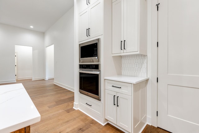 kitchen featuring white cabinets, backsplash, appliances with stainless steel finishes, and light hardwood / wood-style flooring