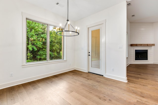 unfurnished dining area featuring a notable chandelier, a large fireplace, and light hardwood / wood-style flooring