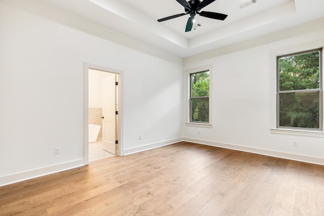 unfurnished room featuring a tray ceiling, ceiling fan, and light hardwood / wood-style floors