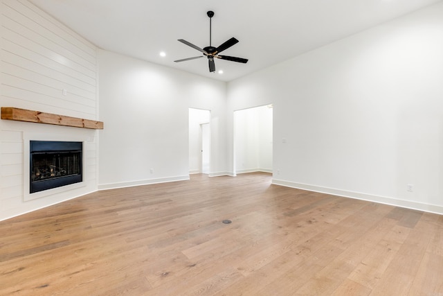 unfurnished living room with ceiling fan, a large fireplace, a towering ceiling, and light hardwood / wood-style flooring