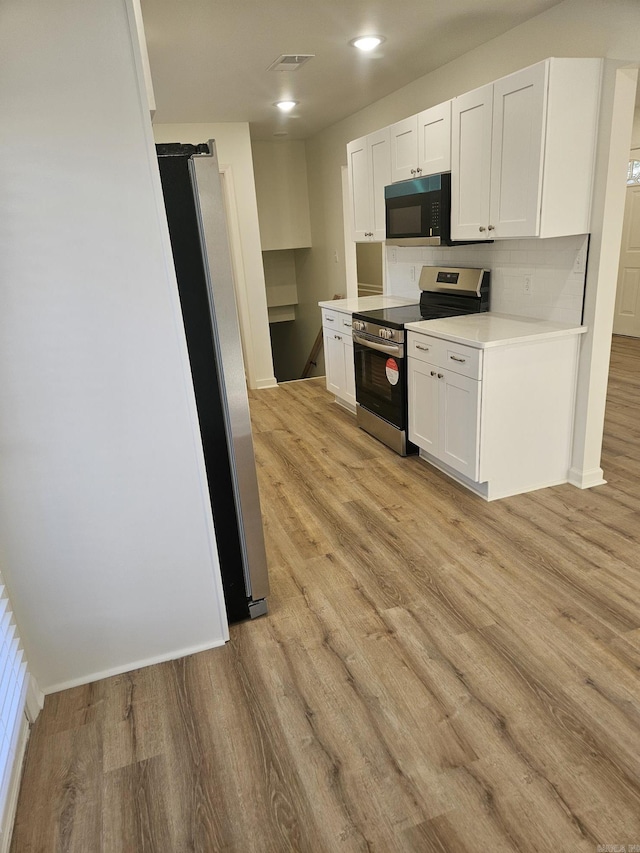 kitchen with white cabinets, light wood-type flooring, stainless steel appliances, and backsplash