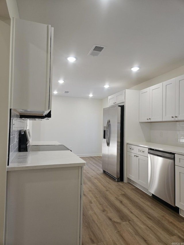 kitchen featuring white cabinets, light wood-type flooring, stainless steel appliances, and tasteful backsplash