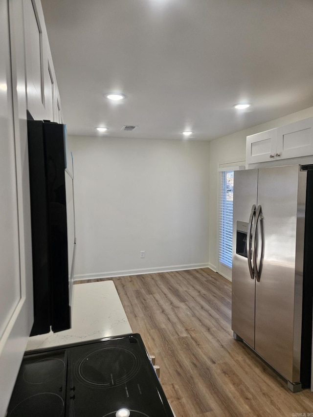 kitchen featuring stainless steel fridge with ice dispenser, electric stove, black refrigerator, white cabinets, and light wood-type flooring