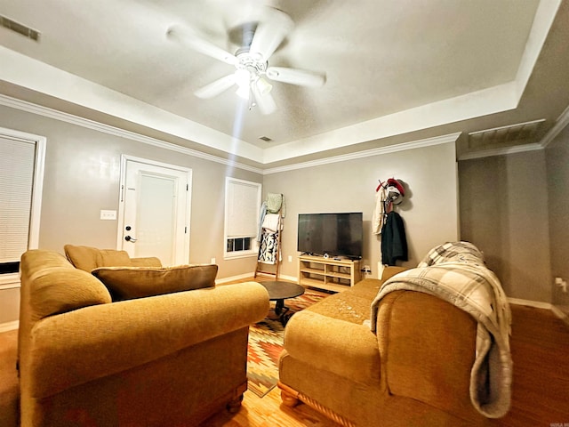 living room with ceiling fan, wood-type flooring, ornamental molding, and a tray ceiling